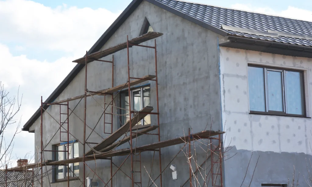 Residential property during K Rend external wall insulation installation with scaffolding in place, showing prepared wall surface ready for basecoat and silicone render application
