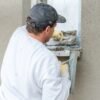 Builder applying wall render around a window, evenly spreading the mortar.
