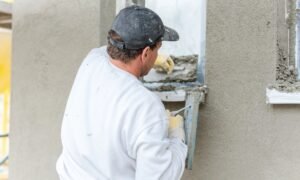 Builder applying wall render around a window, evenly spreading the mortar.