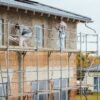 Workers applying cement render to a house wall using tools on a construction site.