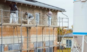 Workers applying cement render to a house wall using tools on a construction site.