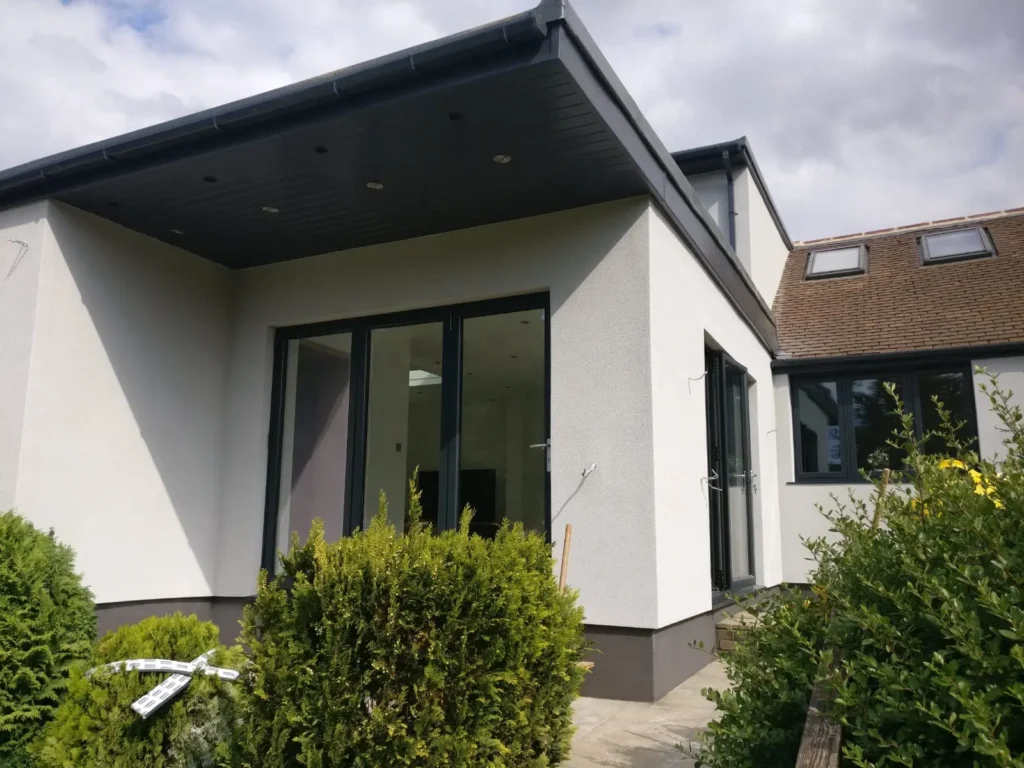 Modern UK home extension showcasing completed external wall insulation with pristine white render finish and dark grey detailing. The professional EWI installation eliminated thermal bridging while creating stunning contemporary appearance.