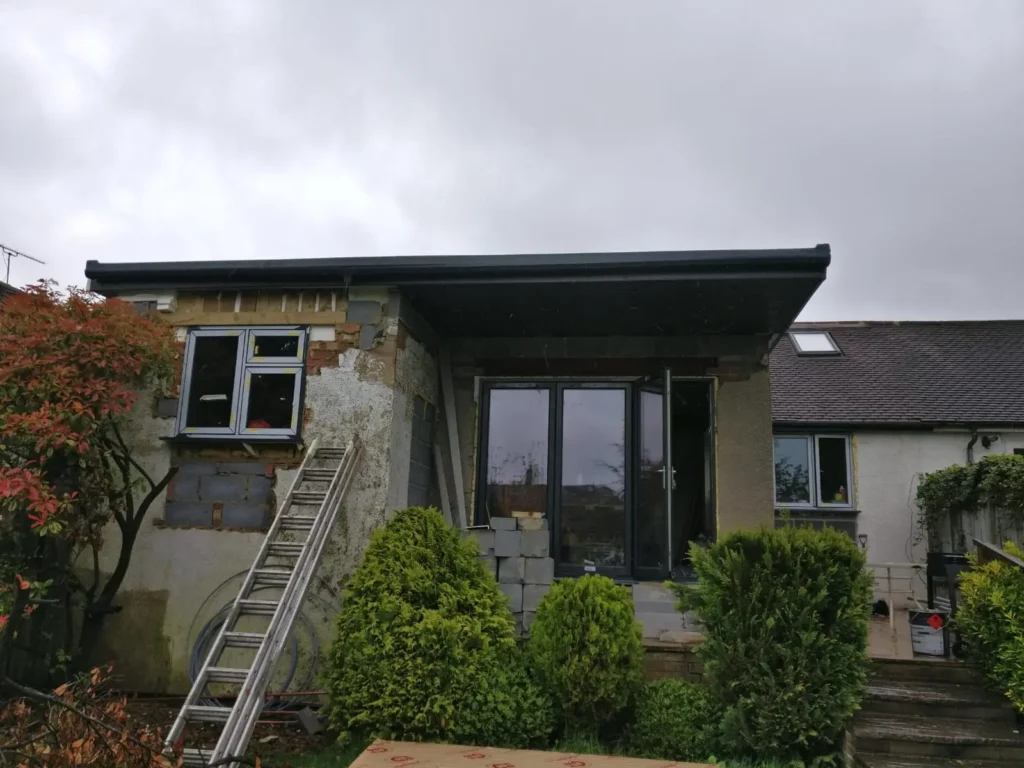 Modern extension before external wall insulation showing raw construction with weathered external walls and ladder access. This image demonstrates the property condition prior to professional EWI installation and transformation.