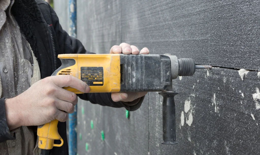 Close-up of EPS insulation panel being drilled into external wall during EWI installation