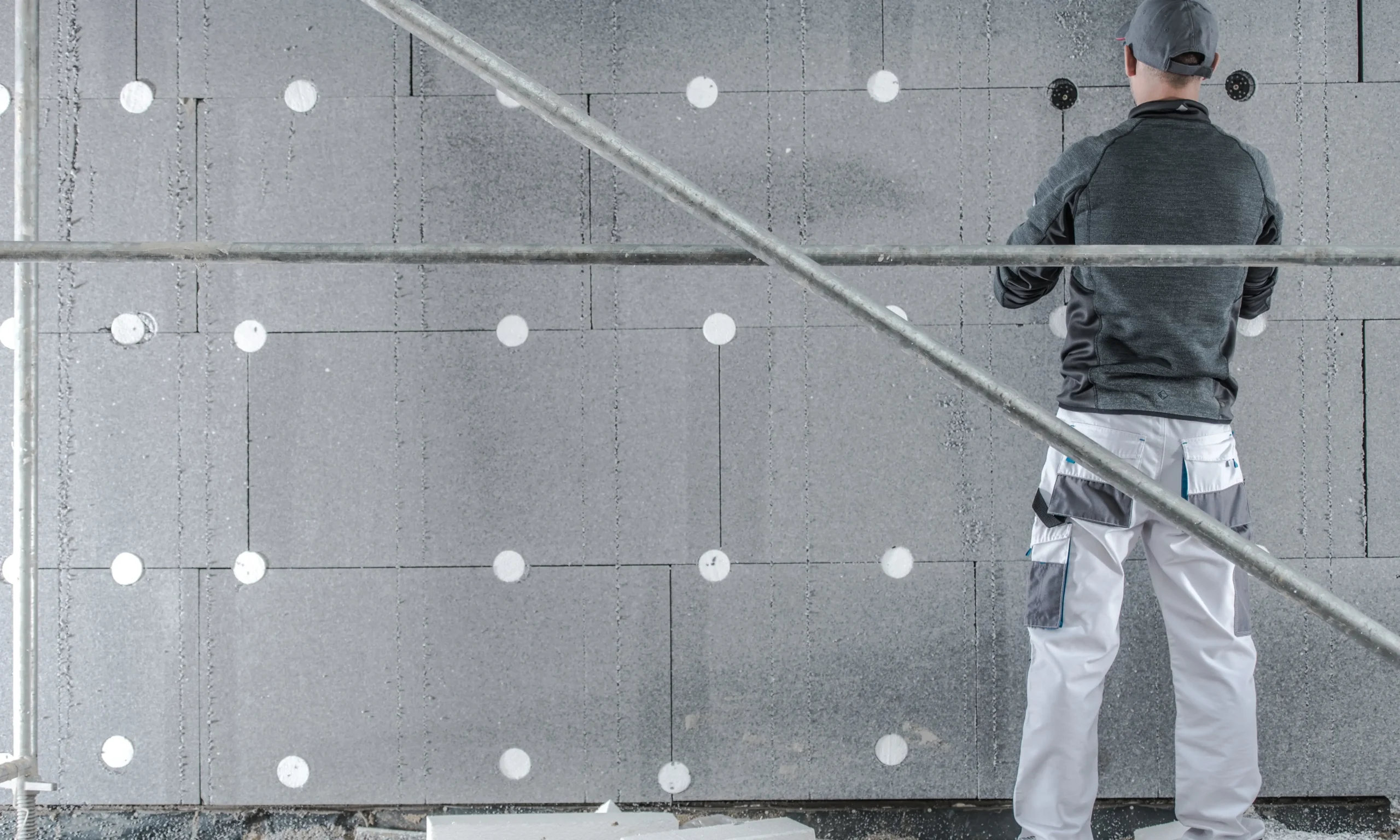 Worker installing graphite EPS insulation panels on exterior wall using fixings