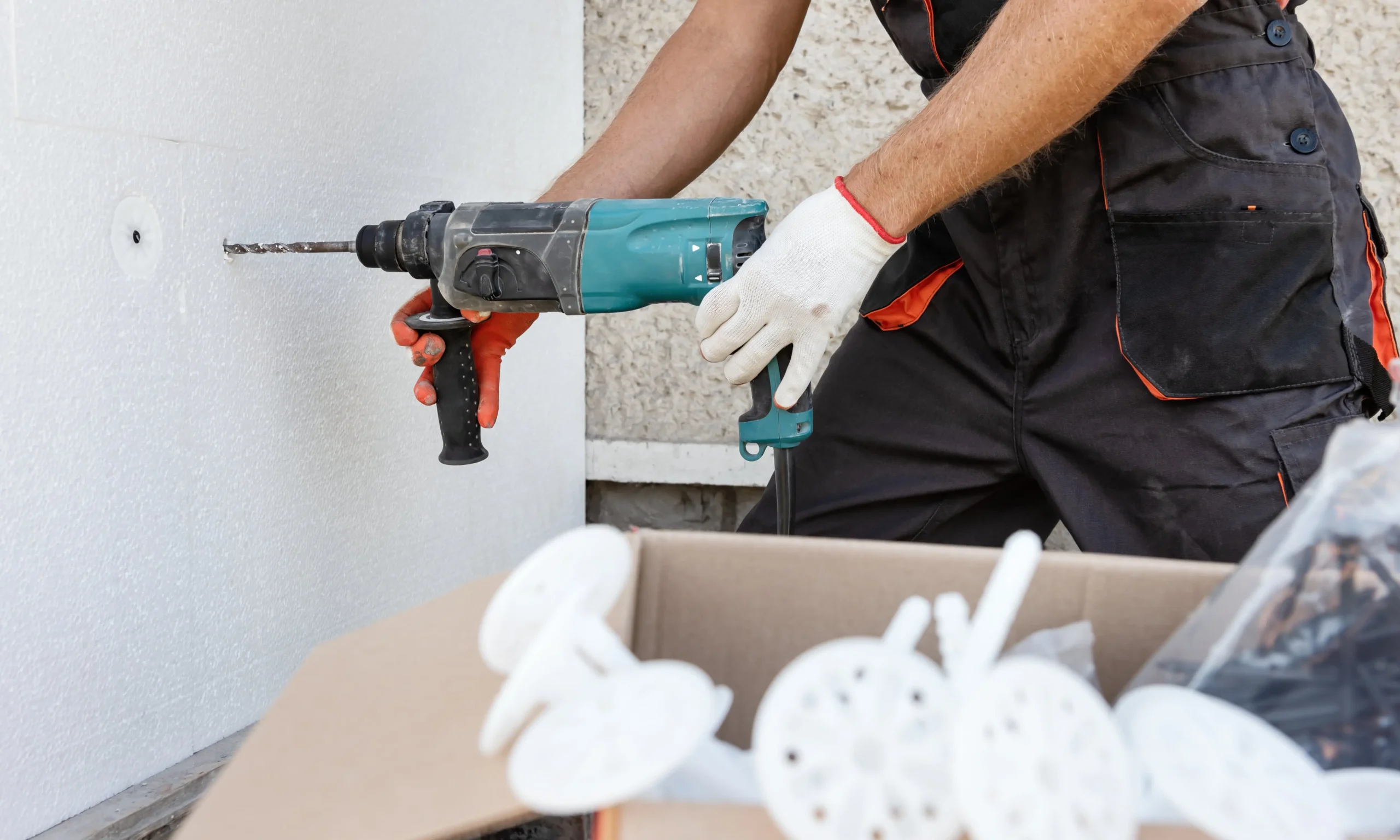 Close-up of a worker using a drill to secure external insulation boards with plastic anchors