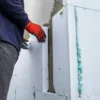 A worker placing polystyrene insulation boards on an exterior wall using adhesive and alignment string
