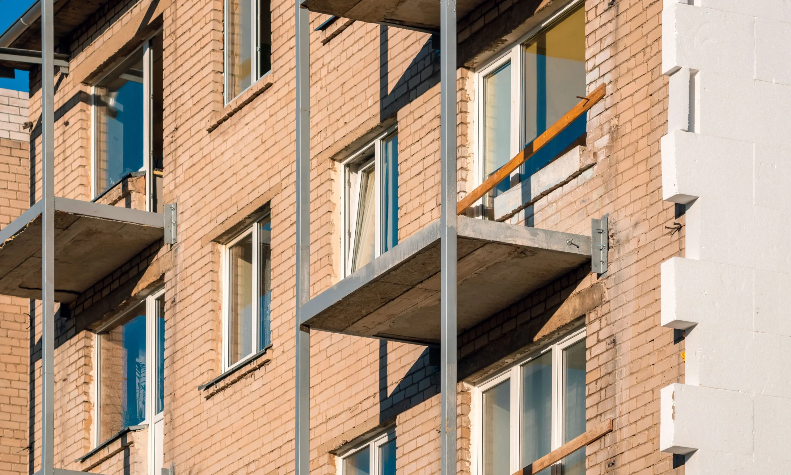 Apartment building facade before external wall insulation, exposed brickwork and concrete balconies visible